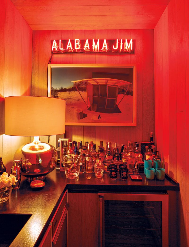 An Alex Hank neon piece, installed above a Los Lichis photograph, casts a glow over the family room’s bar in the home of Zélika García.