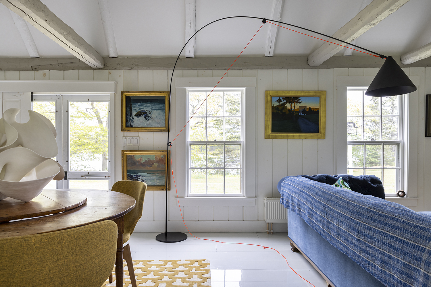 An exuberant European floor lamp sits in front of a trio of paintings of Monhegan Island
