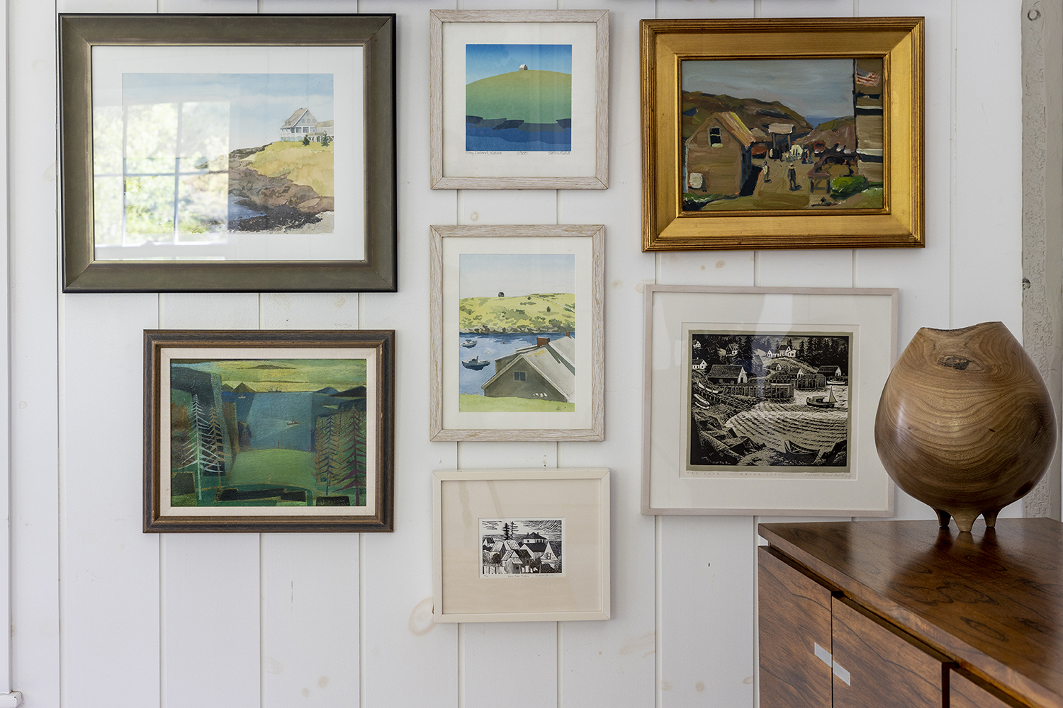 Several works of art completed by Maine artists are framed and hung on a white interior wall.
