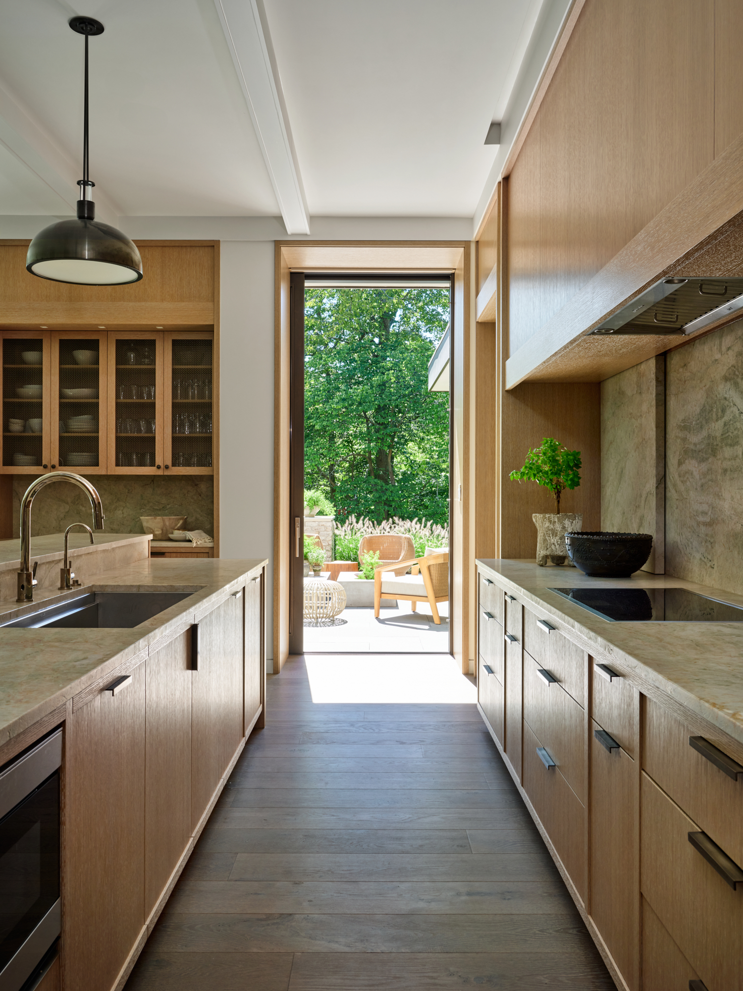 The light-filled kitchen features a harmonious mix of Taj Green quartzite and rift-sawn white oak; the pendants are by Allied Maker, and the sink fittings are by Perrin & Rowe in this renovation by Robbins Architecture