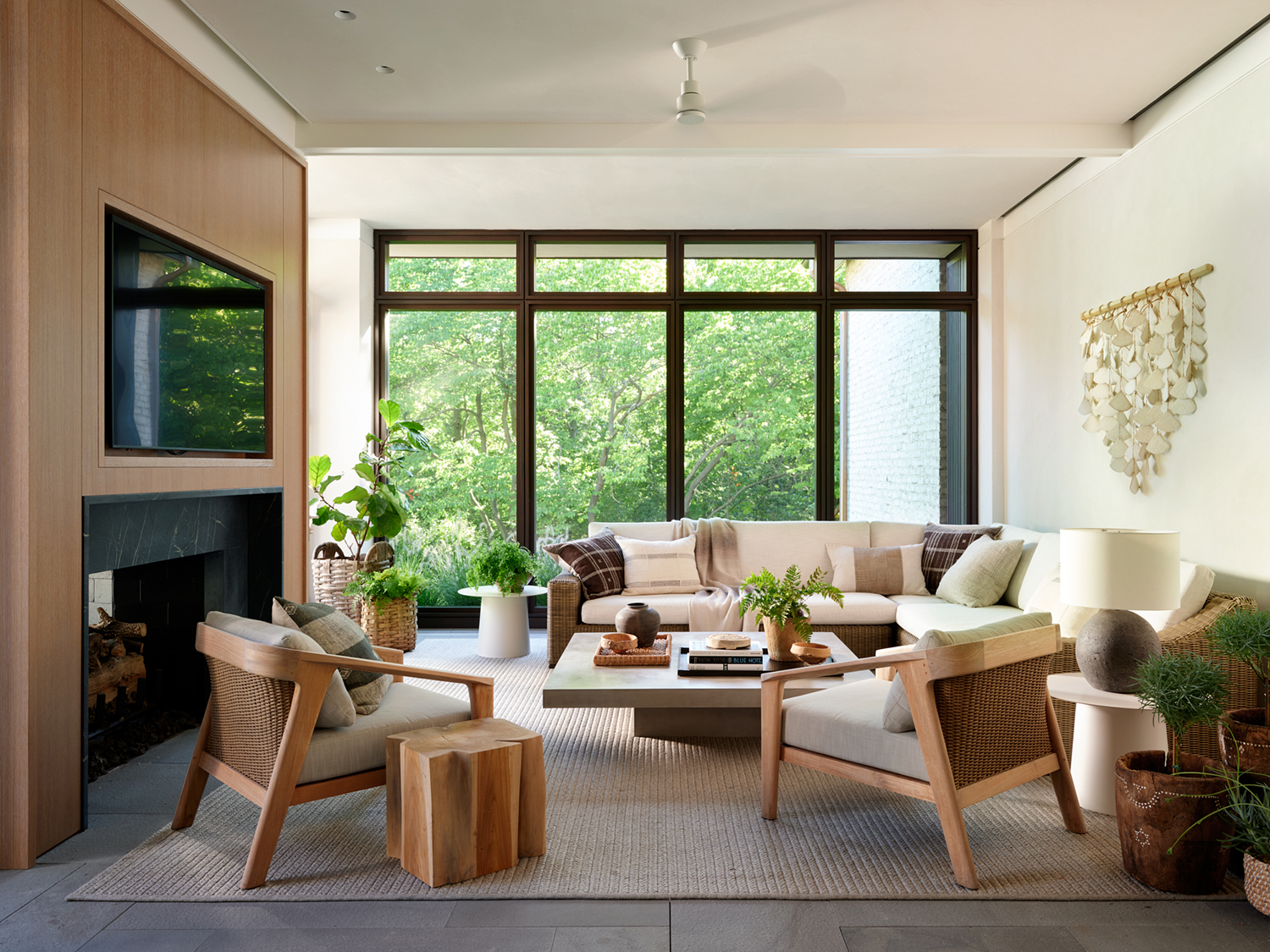 A wall hanging by MQuan Studio graces the screened porch, which also includes RH lounge chairs and a wooden side table by Munder-Skiles in this renovation by Robbins Architecture