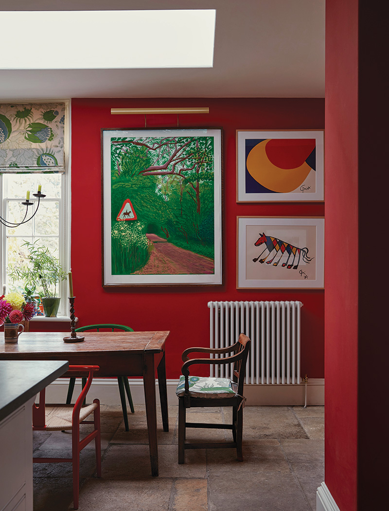 Alexander Calder artworks and a David Hockney landscape from the owners’ collection hang on the kitchen walls, painted in Little Greene’s Atomic Red. The farmhouse dining table was bought at a Christie’s auction, and the antique Carver chair on the end is cushioned in the same Christopher Farr Clothe fabric used for the window shade in the reimagined look crafted by Ben Pentreath.