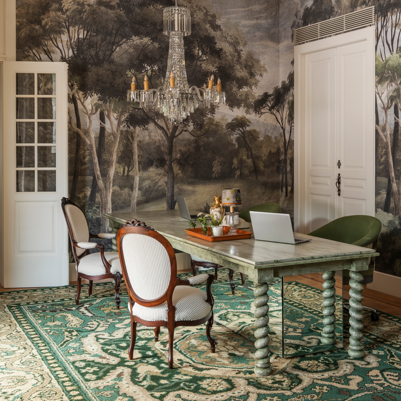 A scenic Ananbô wall covering envelops the reception area at Solar de Vila Meā in Barcelos, Portugal, where a Joana Aranha Signature table is set with antique chairs upholstered in a Pierre Frey fabric and a Crearte swivel chair dressed in a Romo fabric.