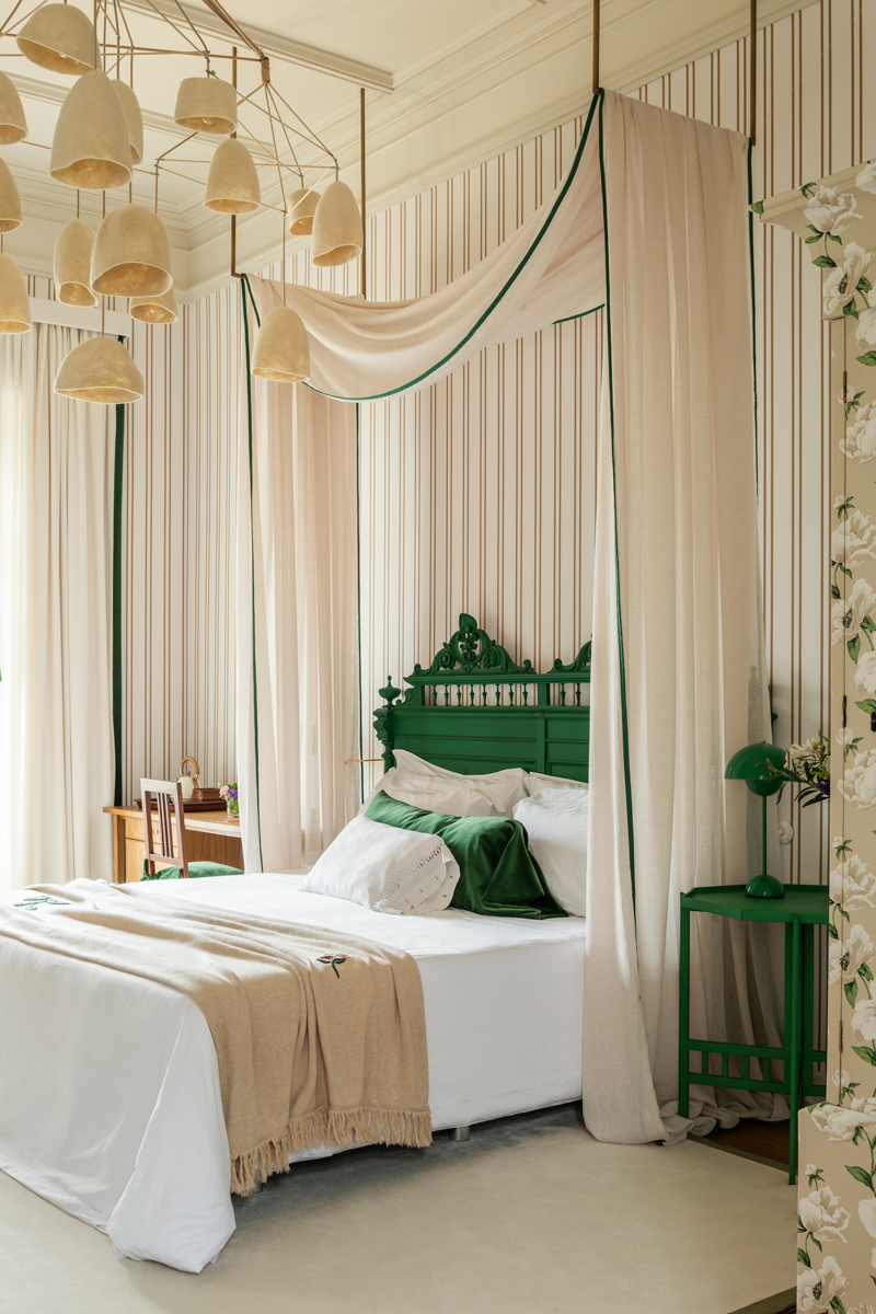 An antique headboard and bedside table painted Green Patina is surmounted by a whimsical light fixture by Po! Paris in one of the bedroom suites designed by Joana Aranha at Solar de Vila Meā in Barcelos, Portugal.