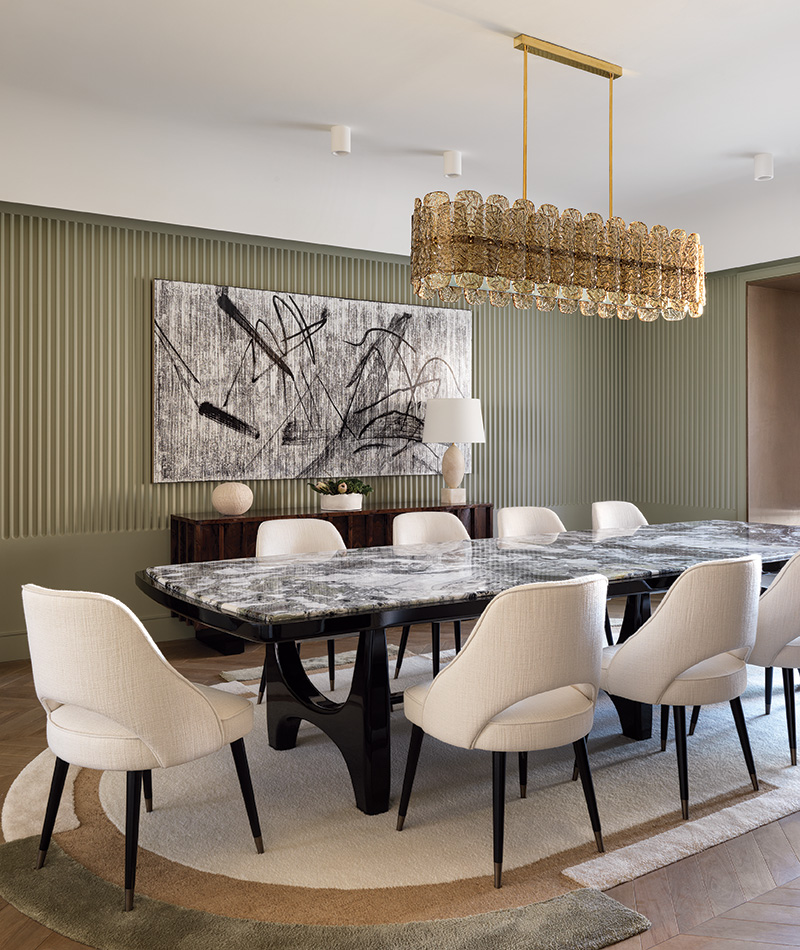 An artwork by Gregor Hildebrandt hangs on a fluted plaster wall in the dining room, which is crowned by a Glustin Luminaires Murano glass light fixture. The table, chairs, sideboard, and rug are all by Damien Langlois-Meurinne.