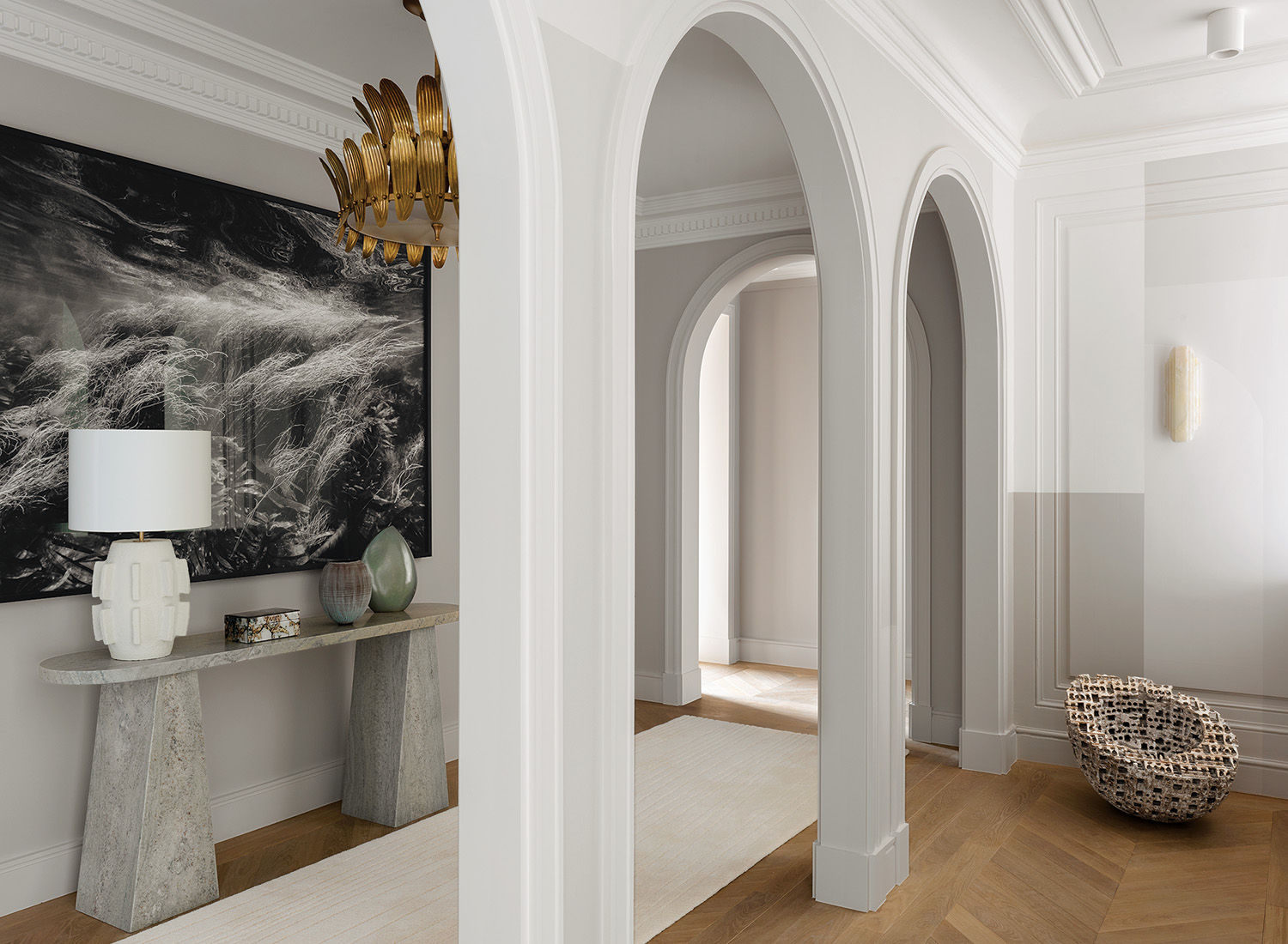 A seascape photograph by Nicolas Floc’h hangs above a Porta Romana lamp and a marble table by Damien Langlois-Meurinne on a stair landing; on the other side of the plaster columns, a Maarten Stuer ceramic sculpture rests beneath a Lisette Rützou sconce.