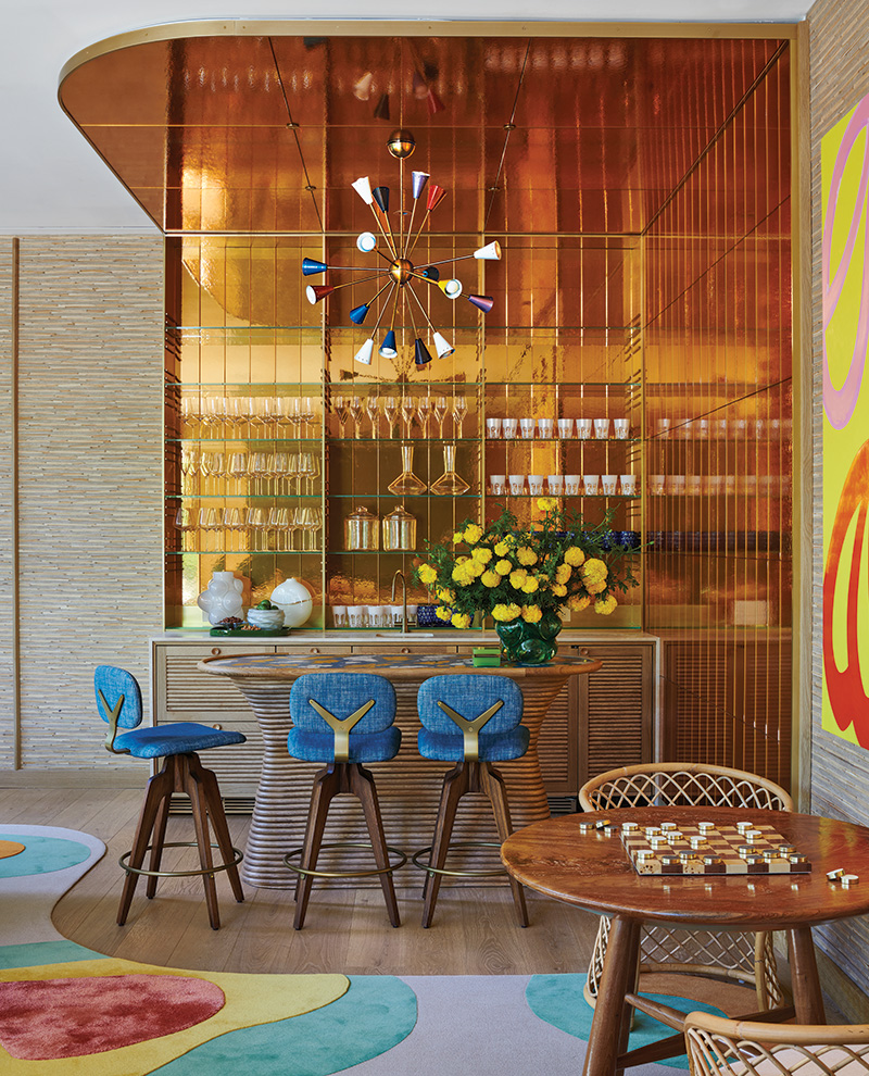 Panels of bronze-toned mirror line the game room area, which features a 1950s Stilnovo chandelier over a bamboo-wrapped bar with seating by Astele in this renovation by William T. Georgis.