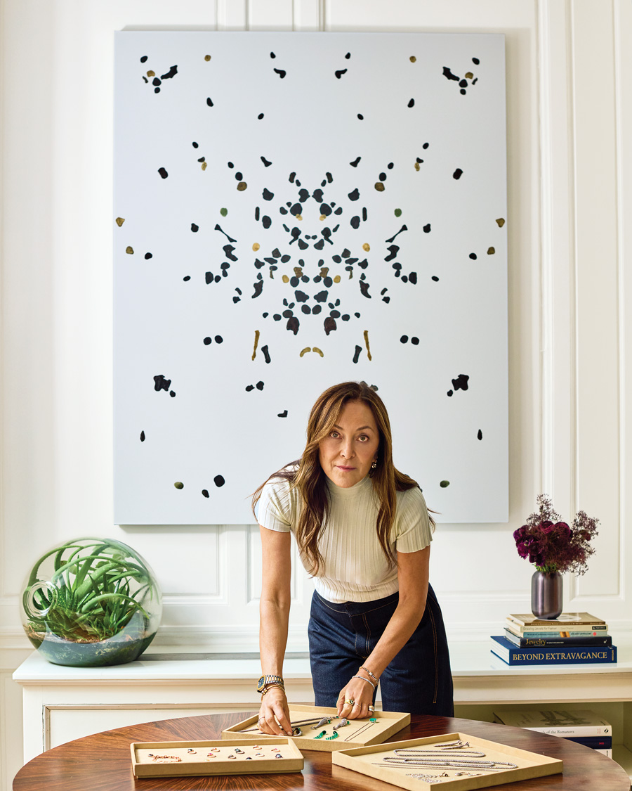 Runsdorf, wearing her All That Is earrings and bracelet, with a selection of trays showcasing her jewelry designs. The painting is by Adam McEwen.