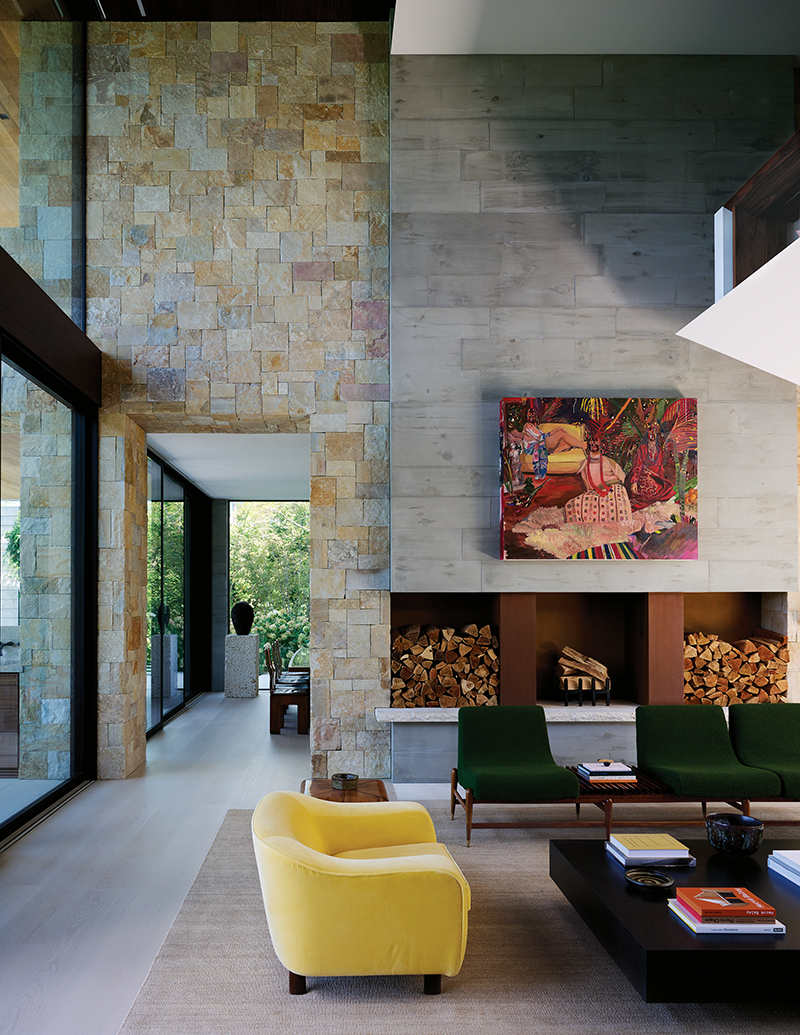 A towering poured-concrete fireplace, which is lined in Cor-Ten steel and accented with a vibrant artwork by Gisela McDaniel, presides over the living room of a house by Ashe Leandro in East Hampton, New York.