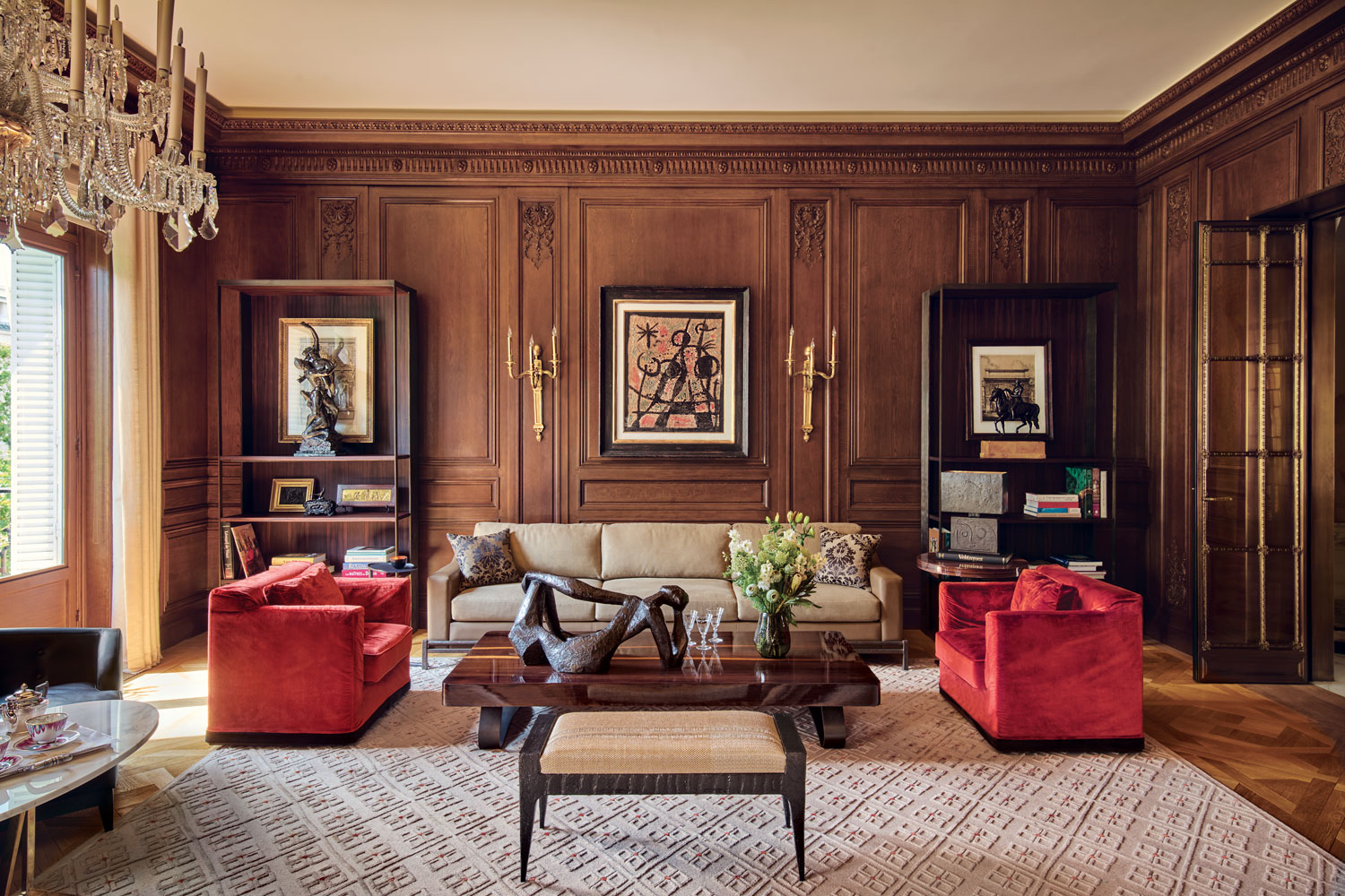 In the first of two living rooms in Aline Hazarian’s Haussmann-era Paris residence, a Joan Miró painting is mounted between 19th-century sconces on paneling by Féau Boiseries. Hazarian designed the sofa and chairs, all upholstered in Dedar fabrics, as well as the stool, the cocktail table that hosts a sculpture by Costas Coulentianos, and the bookshelves, which are topped by antique bronze sculptures. The custom-made rug is by JD Staron.