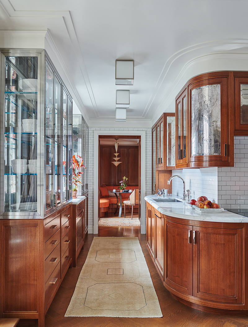 The kitchen features bespoke walnut cabinets with antiqued mirror panels by Stephen Cavallo, Jean Perzel ceiling lights, Waterworks sink fixtures, and a vintage Anatolian runner. A ’30s pendant by Francesco Zecchin and Napoleone Martinuzzi hangs above a custom-made table in the breakfast nook at the back.