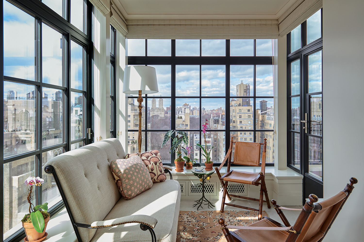 In the guest room conservatory, a ’50s settee attributed to Jacques Adnet and vintage French campaign chairs are grouped with an Alberto Giacometti–style floor lamp by Frances Elkins, a vintage faux-bois side table, and a Turkish Deco rug from Nazmiyal.