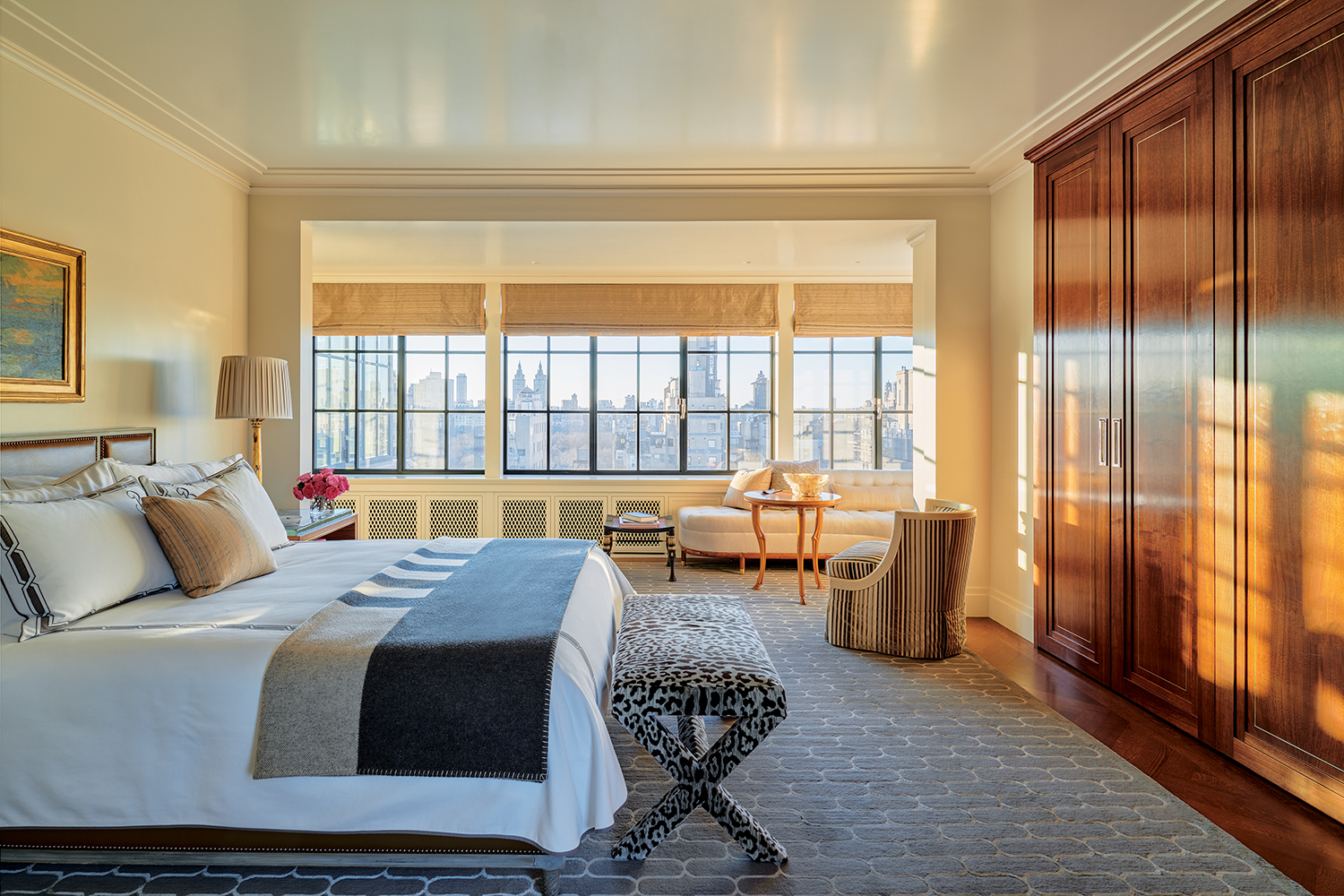 A painting by Frederick J. Mulhaupt overlooks the primary suite’s custom bed; Lee Ledbetter & Associates designed the bench clad in a Clarence House jaguar print, the waxed-walnut closets with nickel-plated brass inlays, the rug, and the window banquette, which is joined by a T. H. Robsjohn-Gibbings side table from 1940.