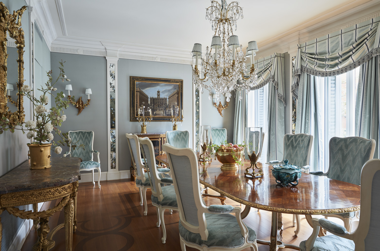 Mirrored pilasters painted by Delphine Nény add dimension to the dining room. Cowtan & Tout fabrics were used for the walls and curtains, and the table is vintage Jansen from Christie’s Paris. The Italian ormolu and cut-crystal chandelier are from Christie’s.