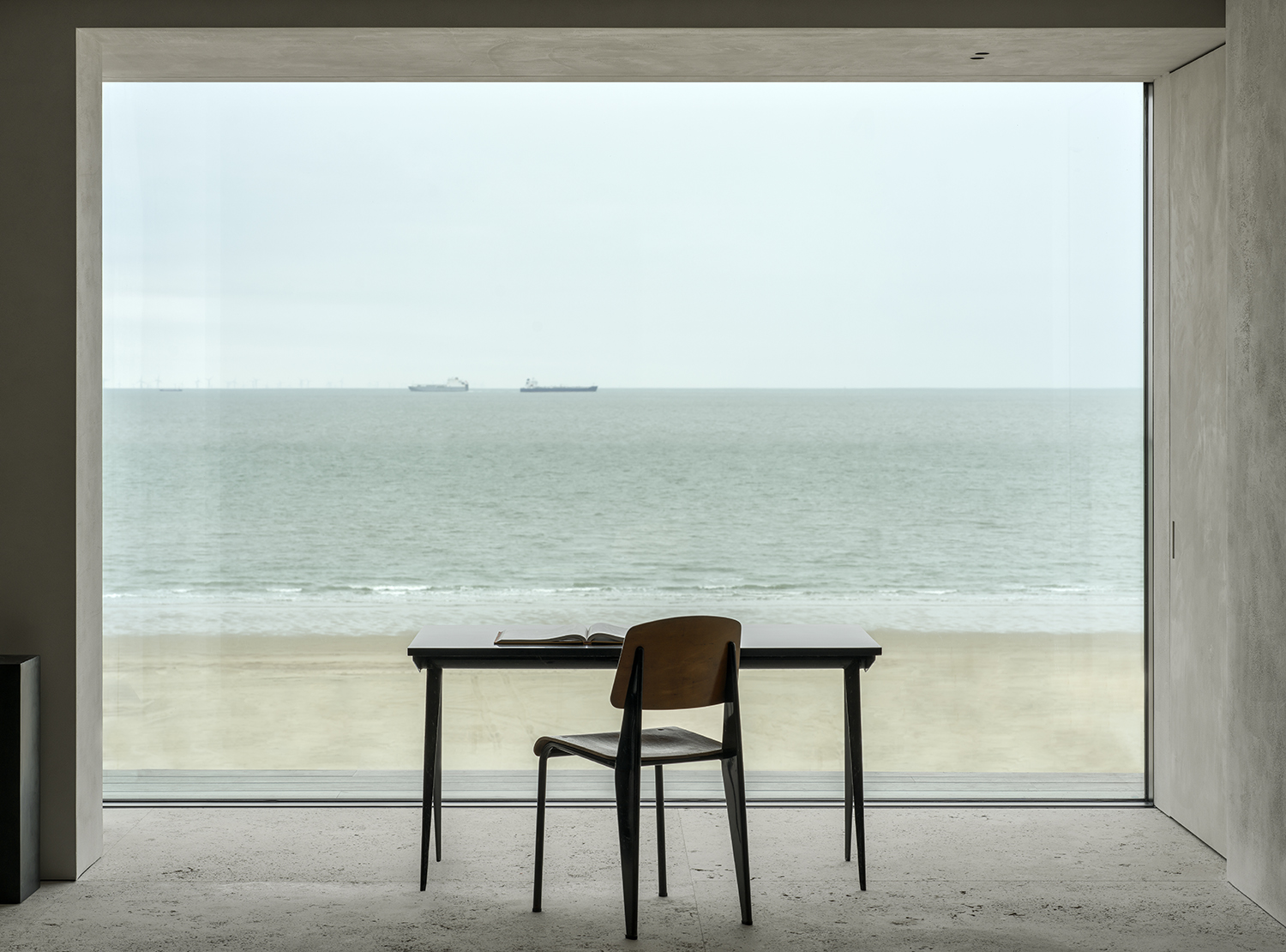 A vintage Jean Prouvé desk and chair create a contemplative workspace before the sea view for this DH Apartment in Knokke, Belgium.