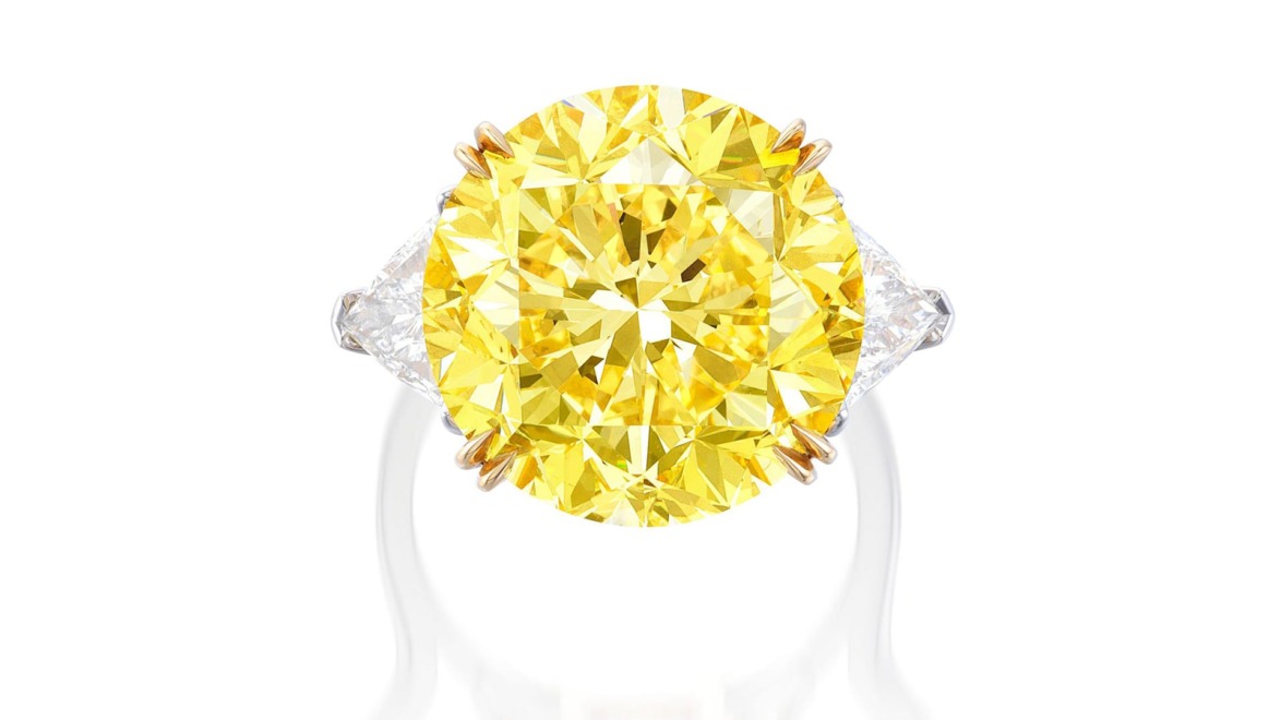 Yellow diamond ring with white triangular side stones and a white band, displayed on a white background.