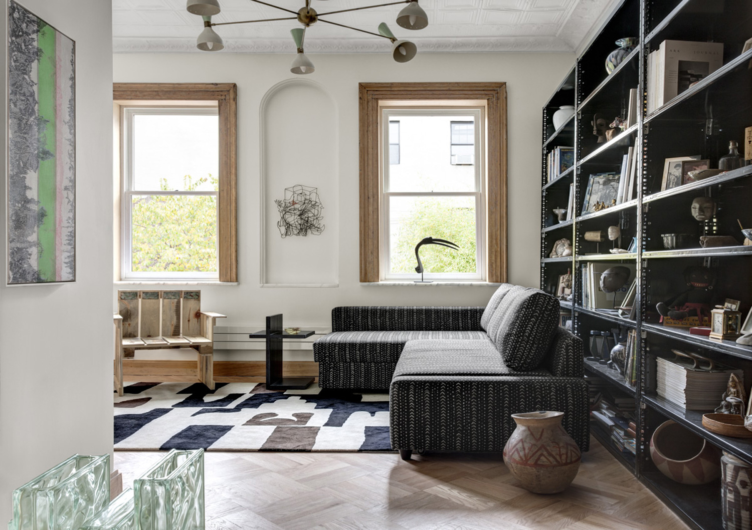 Ceiling-height industrial shelving houses a collection of photographs, artifacts, and keepsakes in the library, where a sectional upholstered in African mudcloth fabric is perched atop a custom wool and silk rug.