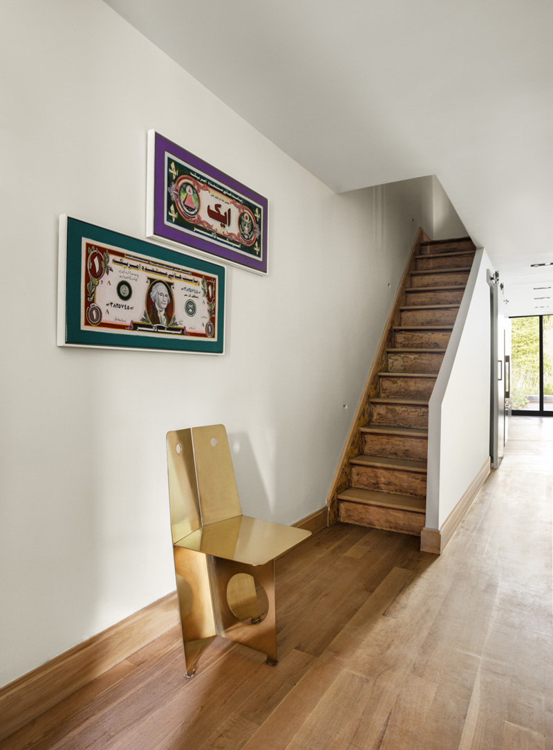 A brass chair by Lionel Jadot sits beneath a pair of paintings by Adnan Ali Manganhar that satirize the U.S. Dollar.