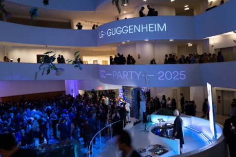 People gather at a modern, multi-level building event with blue lighting and an illuminated sign displaying LG and Guggenheim.